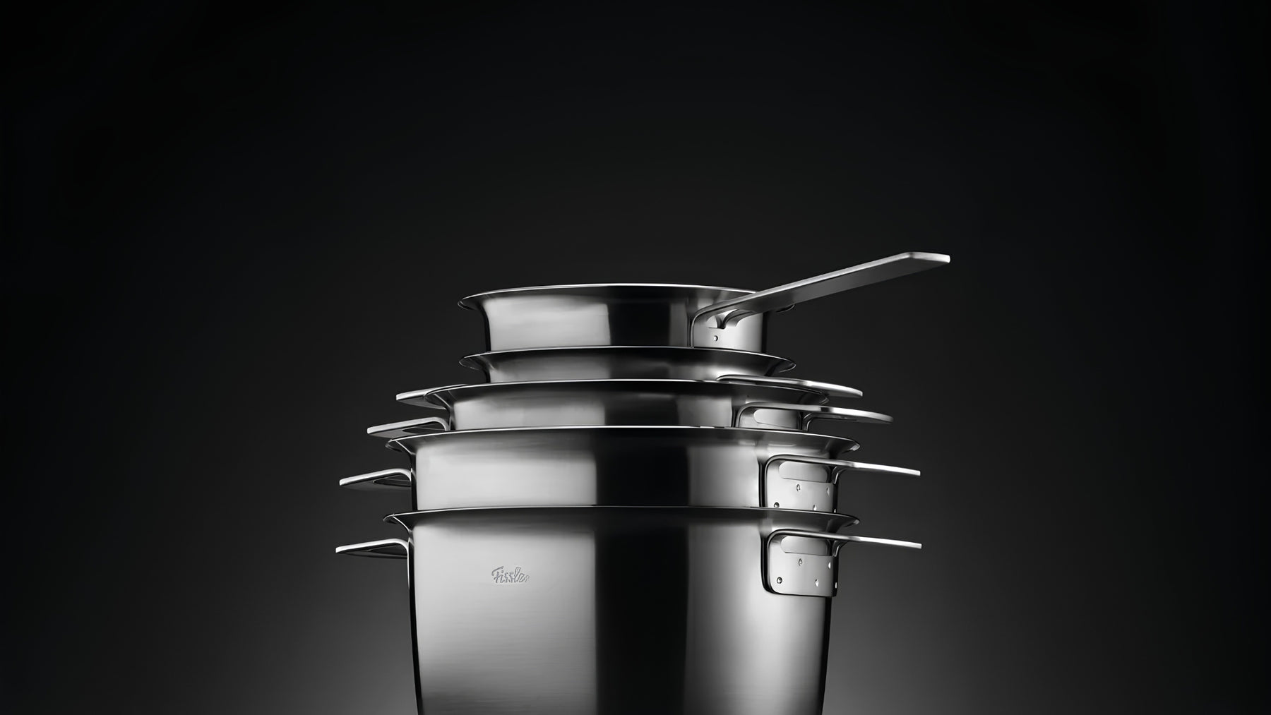 Stacked Fissler stainless-steel cookware against a dark background.